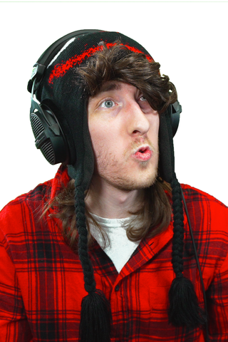 KreekCraft, wearing his signature black and red winter hat with ear flaps and braided tassels. He is also wearing large black headphones, a red and black checkered shirt, and has a surprised expression on his face. The background is plain white.
