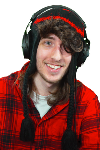 KreekCraft, wearing his signature black and red winter hat with ear flaps and braided tassels. He is also wearing large black headphones, a red and black checkered shirt, and has a surprised expression on his face. The background is plain white.